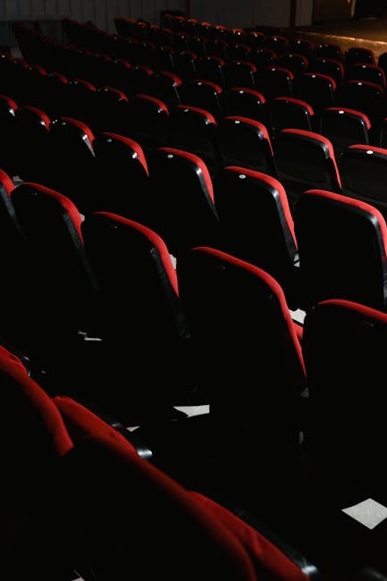 Interior view of the Queens Theatre Hornchurch auditorium showing rows of red and black upholstered seats arranged in an orderly fashion. The seats are clean and free of dust, with the red fabric upho