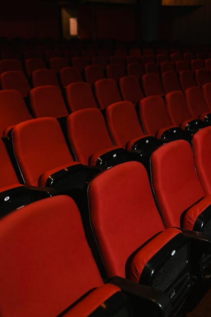 Interior view of the Queens Theatre Hornchurch auditorium showing rows of red and black upholstered seats arranged in an orderly fashion. The seats are clean and free of dust, with the red fabric upho
